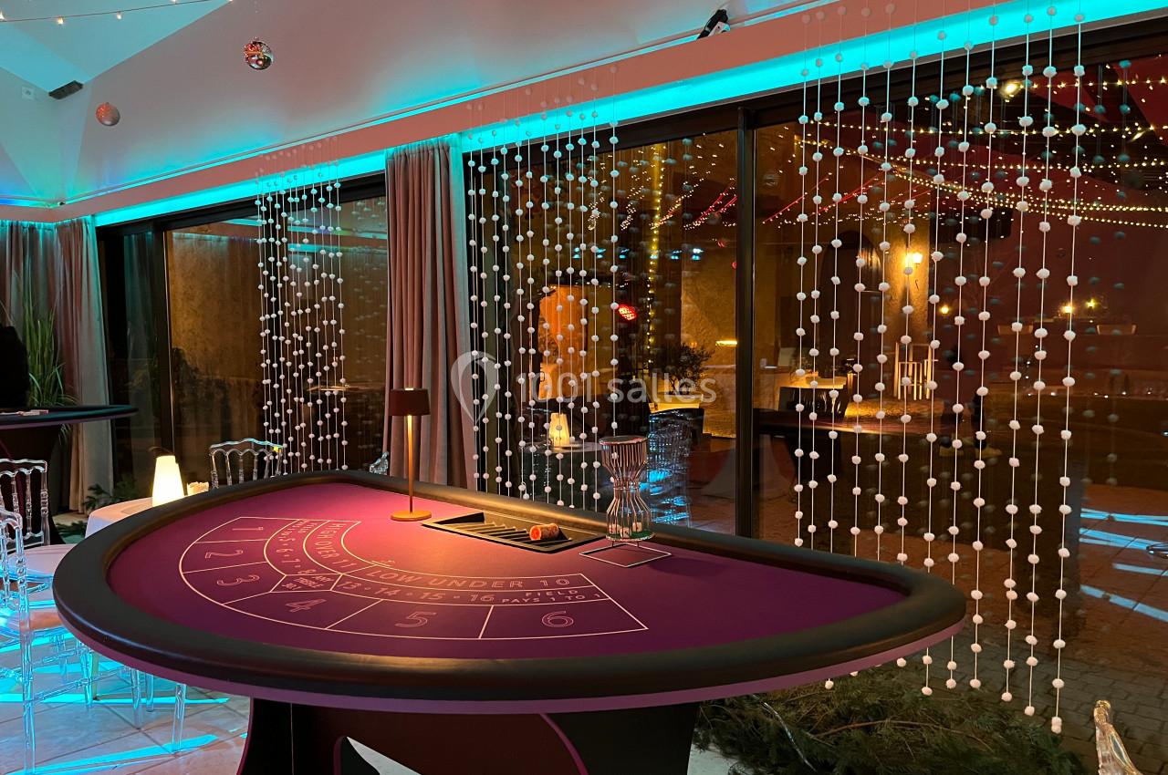 Table de jeu de casino avec tapis violet dans une salle décorée de guirlandes lumineuses et baies vitrées.