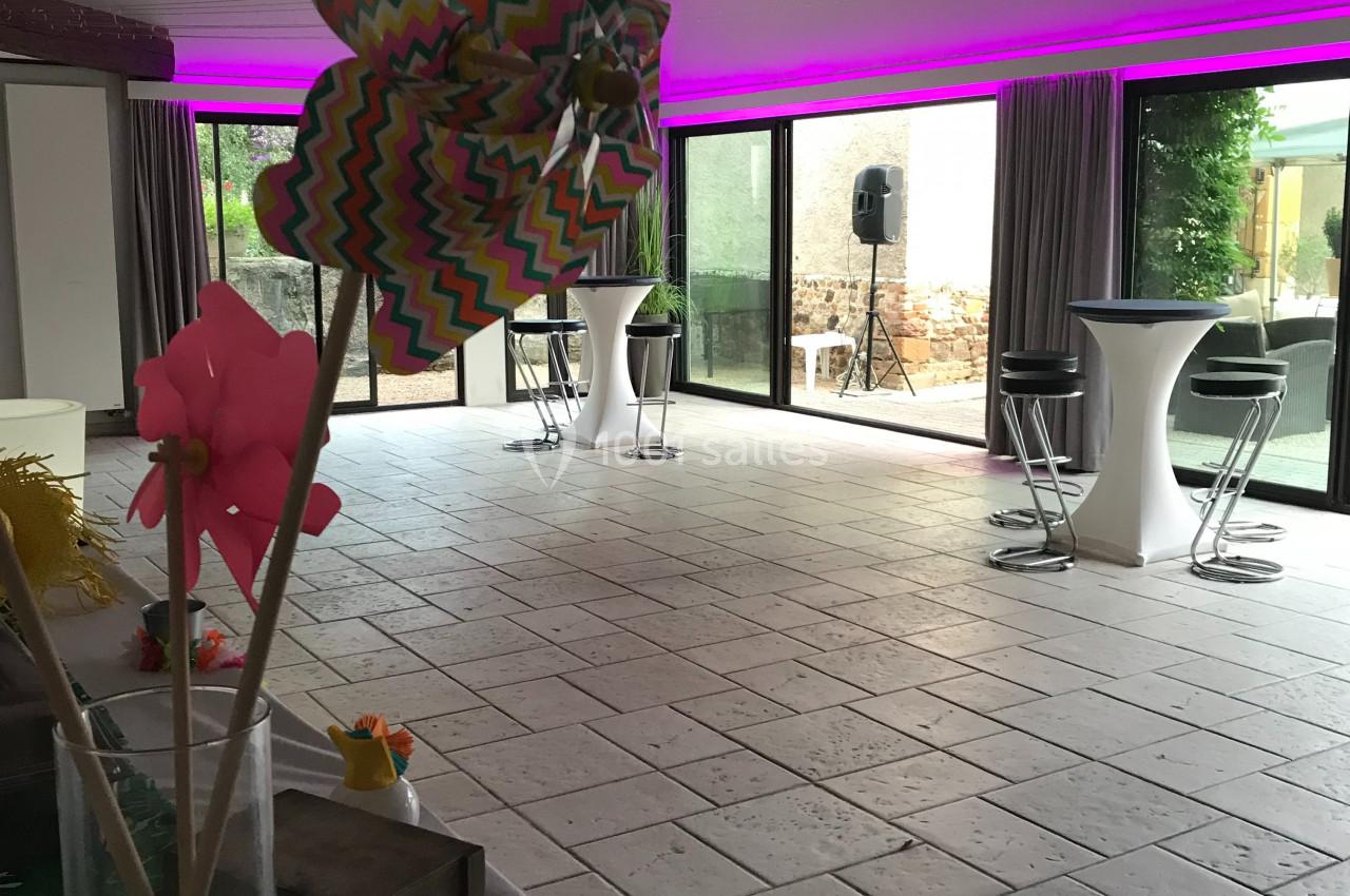 Salle lumineuse avec grandes baies vitrées, décoration colorée et mobilier moderne sous un plafond avec poutres apparentes.