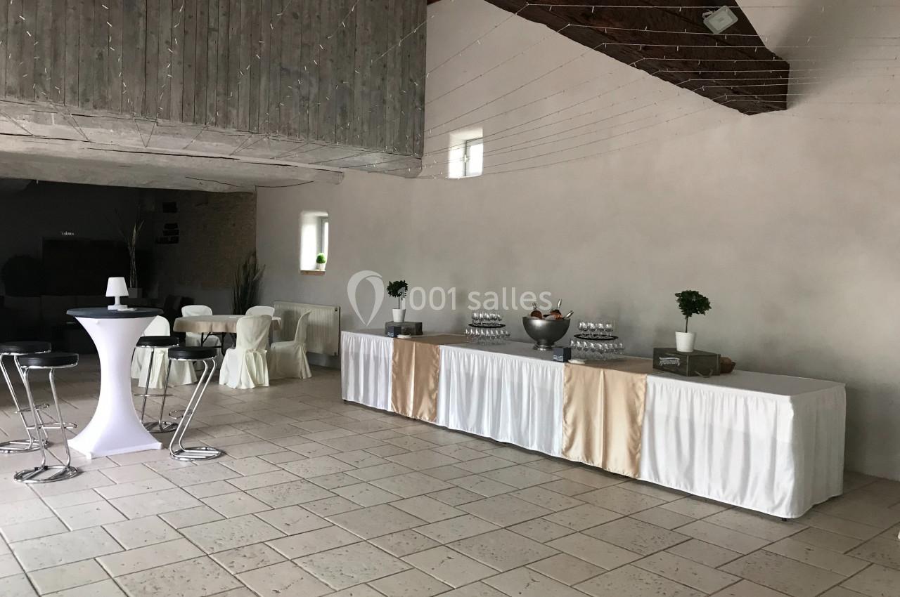 Salle de réception avec tables hautes, chaises, et une grande table décorée pour un buffet.
