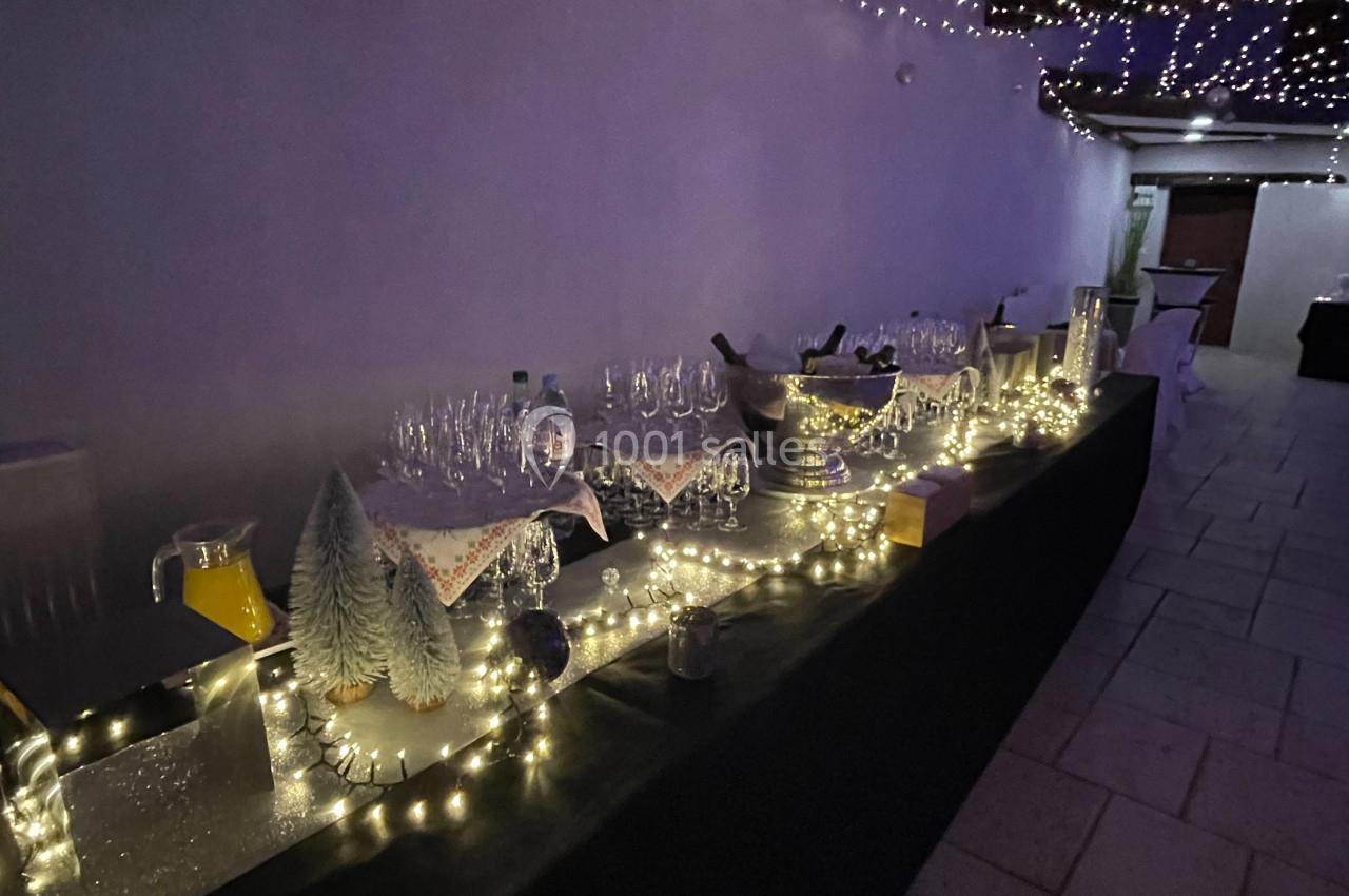 Table décorée avec guirlandes lumineuses, verres et carafes, dans un espace couvert avec éclairage tamisé.