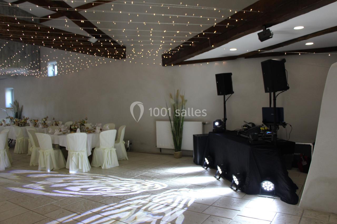 Salle de réception décorée avec des guirlandes lumineuses, tables dressées et espace DJ équipé de matériel audio.