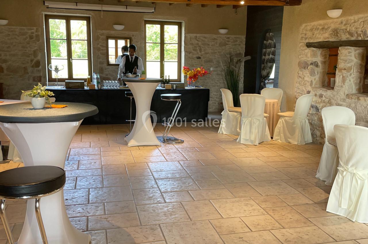 Salle lumineuse avec tables hautes, chaises habillées de housses blanches, et un buffet en arrière-plan.