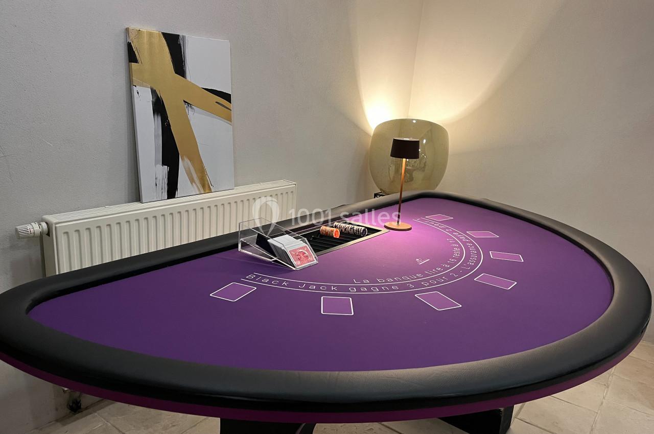 Table de blackjack violette avec cartes, jetons et lampe allumée dans un coin de pièce sobrement décoré.