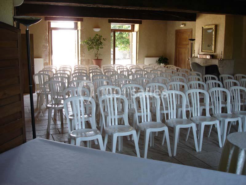 Salle avec des rangées de chaises blanches en plastique alignées, éclairée par la lumière naturelle provenant des fenêtres.