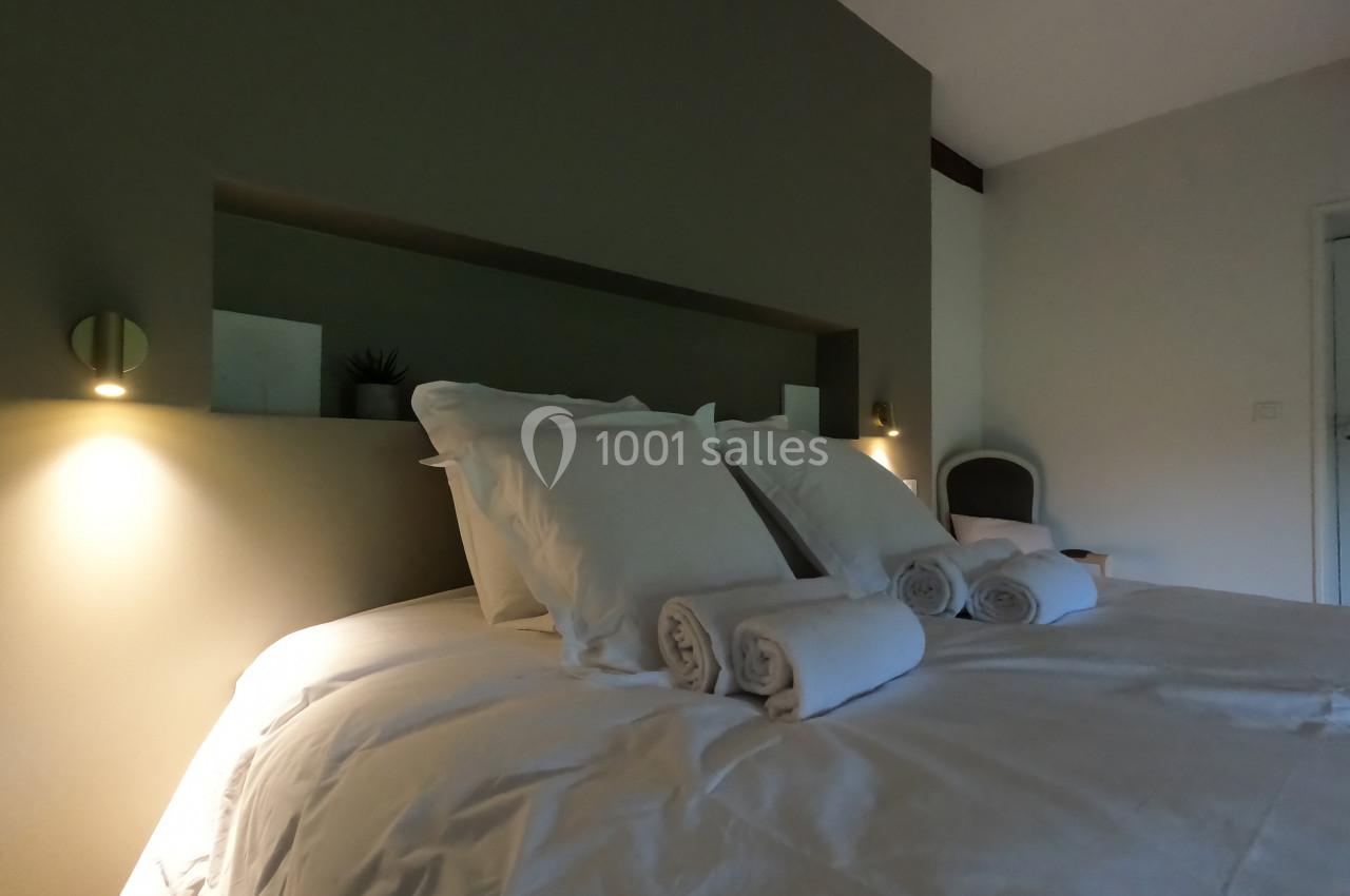 Lit double avec draps blancs, oreillers et serviettes roulées, éclairé par deux appliques murales dans une chambre sobre.