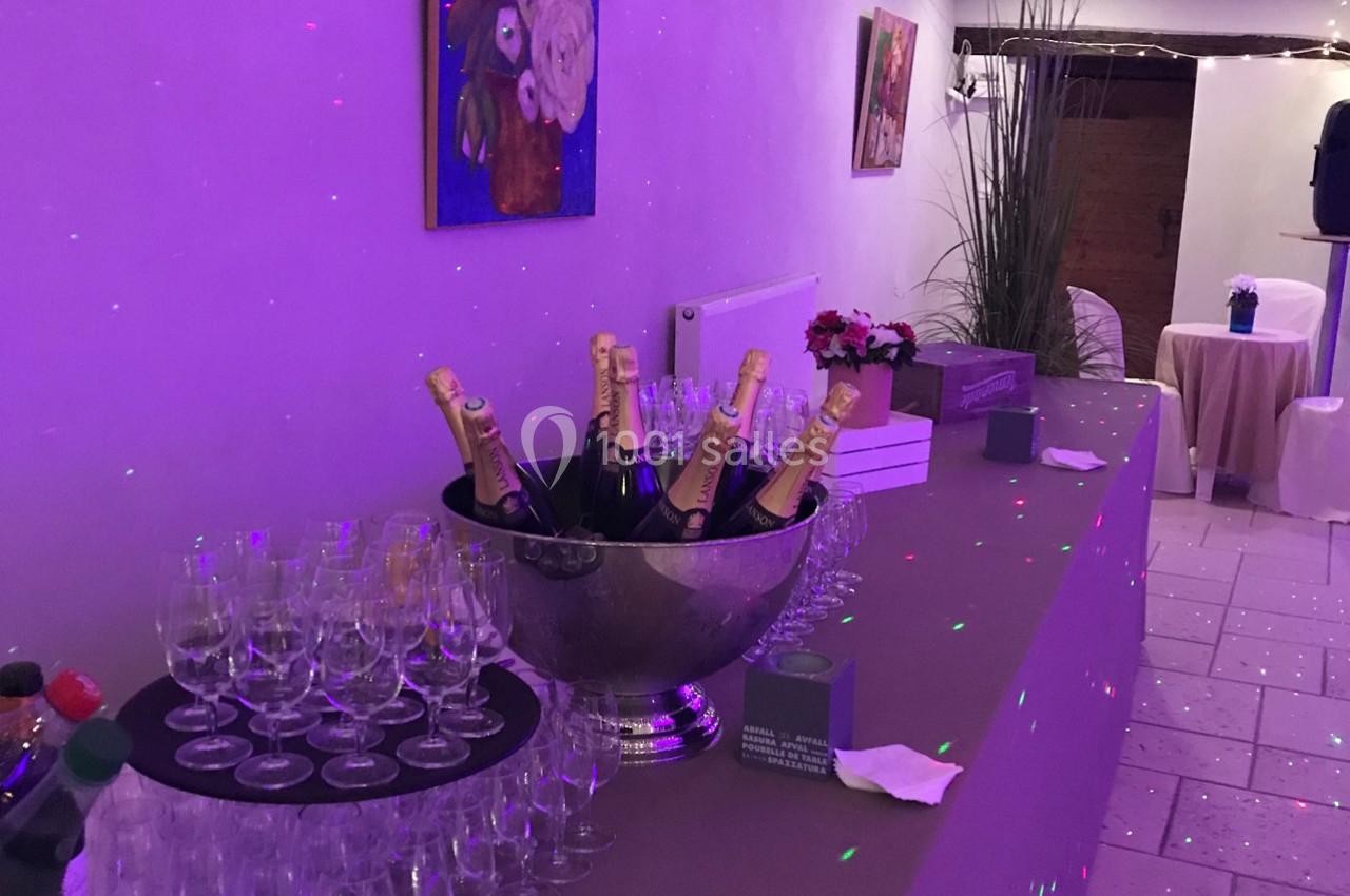 Table décorée avec des bouteilles de champagne dans un seau, verres alignés et éclairage violet dans une salle.