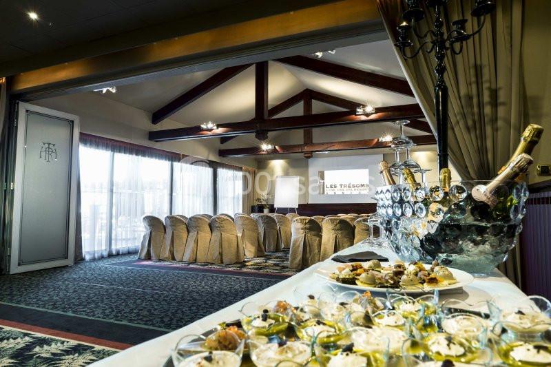 Salle de réception avec chaises alignées, écran de projection et table garnie de plats et bouteilles de champagne.