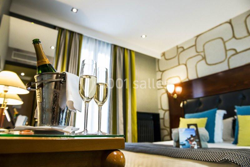 Seau à champagne avec deux flûtes sur une table, devant un lit dans une chambre d'hôtel lumineuse et élégante.