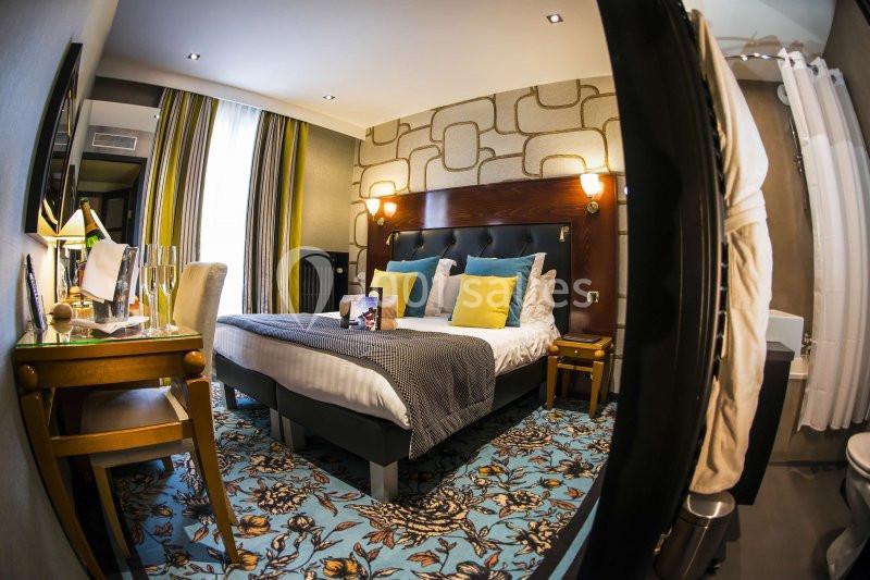 Chambre d'hôtel avec lit double, coussins colorés, bureau, éclairage chaleureux et décoration moderne.