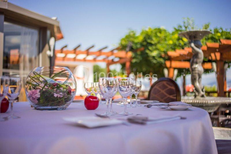 Table dressée en extérieur avec des verres, des couverts, un centre de table floral et une statue en arrière-plan.