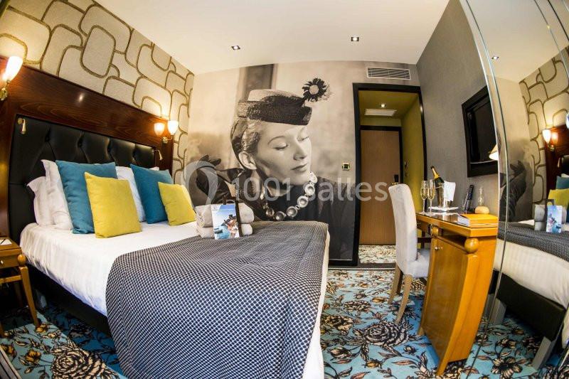 Chambre d'hôtel avec lit double, coussins colorés, bureau, miroir et décoration murale en noir et blanc.