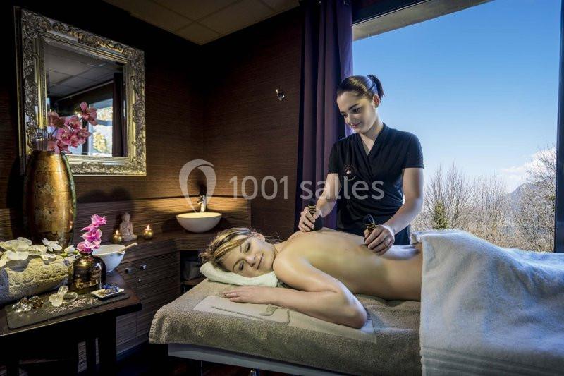 Une femme reçoit un massage relaxant dans une salle de spa lumineuse avec vue sur un paysage extérieur.