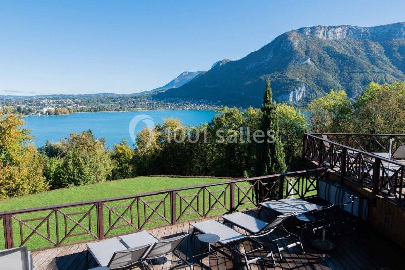Vue sur un lac entouré de montagnes, avec une terrasse en bois équipée de chaises longues au premier plan.