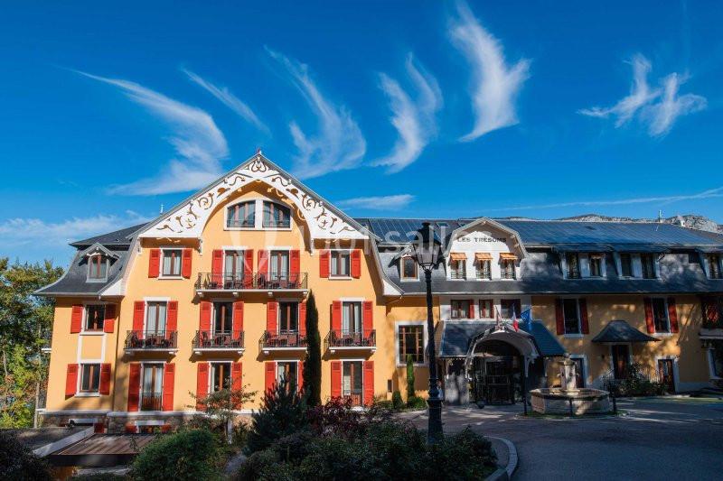 Façade d'un bâtiment coloré avec volets rouges, ciel bleu et nuages en arrière-plan.
