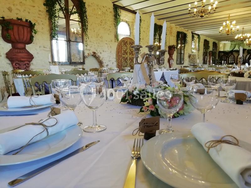 Table dressée avec nappes blanches, vaisselle élégante et décoration florale dans une salle de réception rustique.