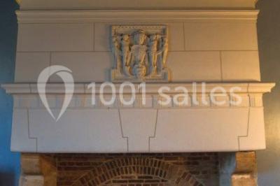 Cheminée ancienne en pierre avec un bas-relief sculpté, encadrée par un mur bleu et un plafond en bois.