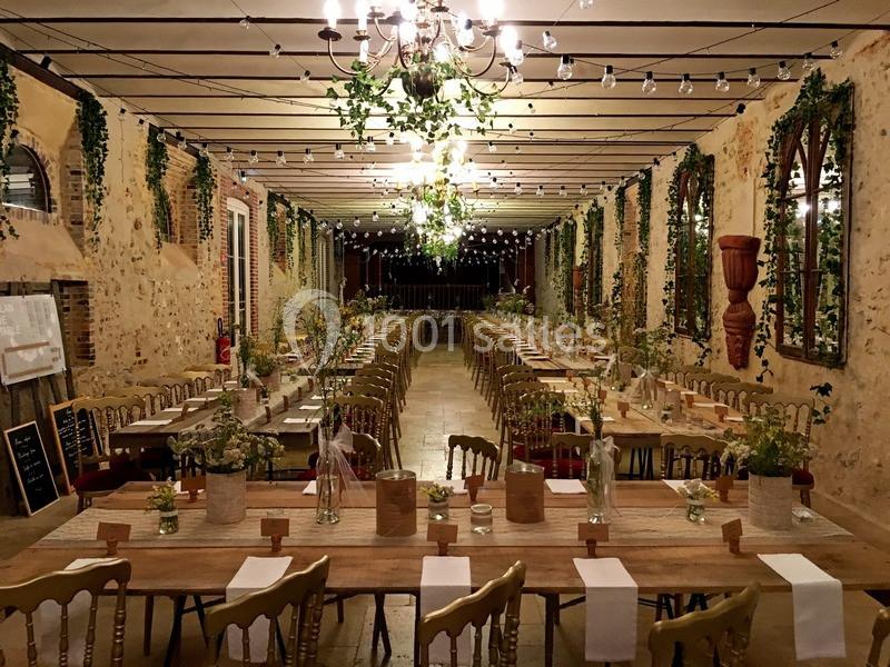 Grande salle de réception décorée avec des guirlandes lumineuses, des tables en bois et des plantes suspendues.