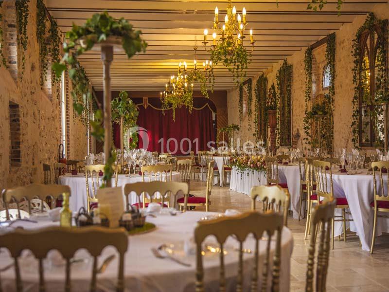 Salle de réception décorée avec des tables dressées, des chaises dorées et des guirlandes végétales suspendues.