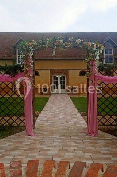Allée pavée menant à une porte d'entrée, encadrée par une arche fleurie et des rideaux roses.