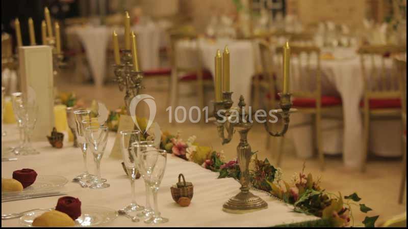 Salle de réception décorée avec des chandeliers, des verres et des fleurs sur une table dressée élégamment.