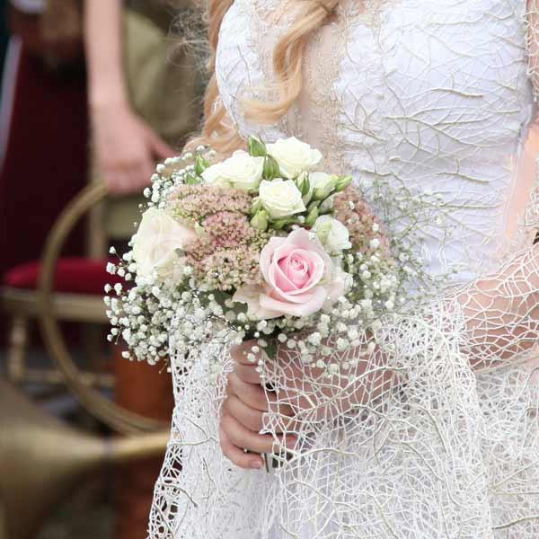 Une mariée en robe blanche tient un bouquet de fleurs roses et blanches avec des touches de gypsophile.