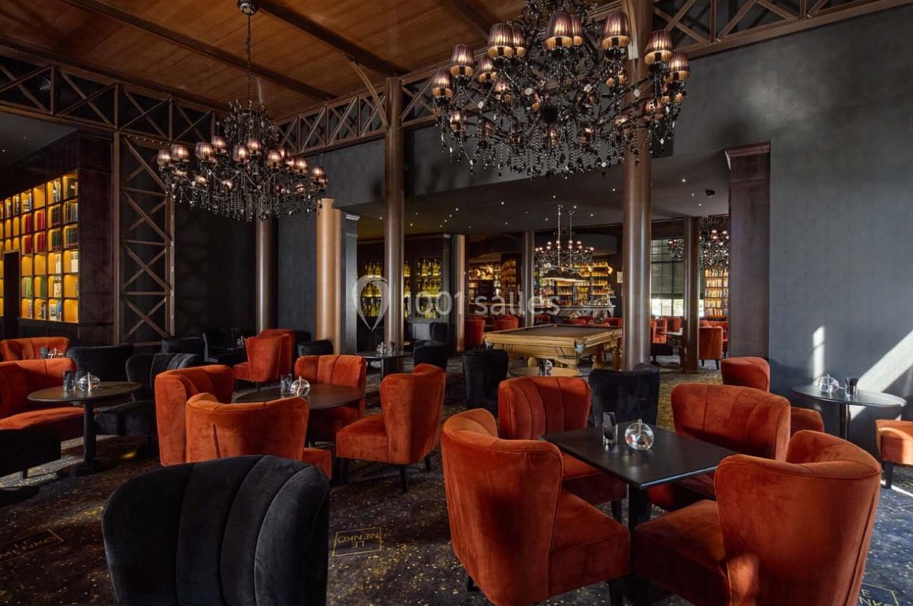 Salle élégante avec fauteuils orange et noirs, lustres en cristal, murs sombres et étagères illuminées en arrière-plan.