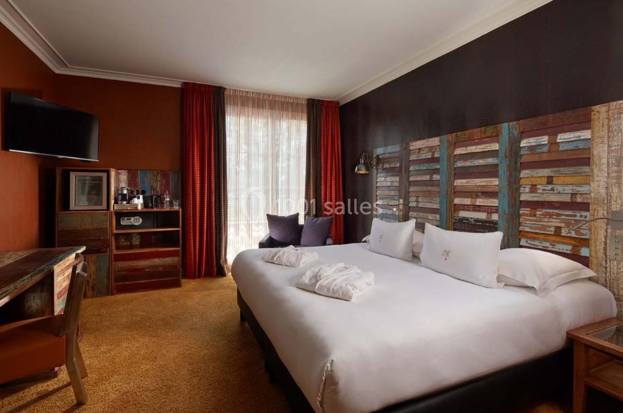 Chambre d'hôtel avec lit double, bureau, télévision murale, fauteuils, et décoration aux tons chauds et boisés.