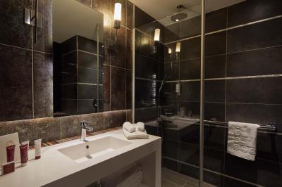 Salle de bain moderne avec lavabo blanc, douche vitrée, murs carrelés sombres et éclairage chaleureux.