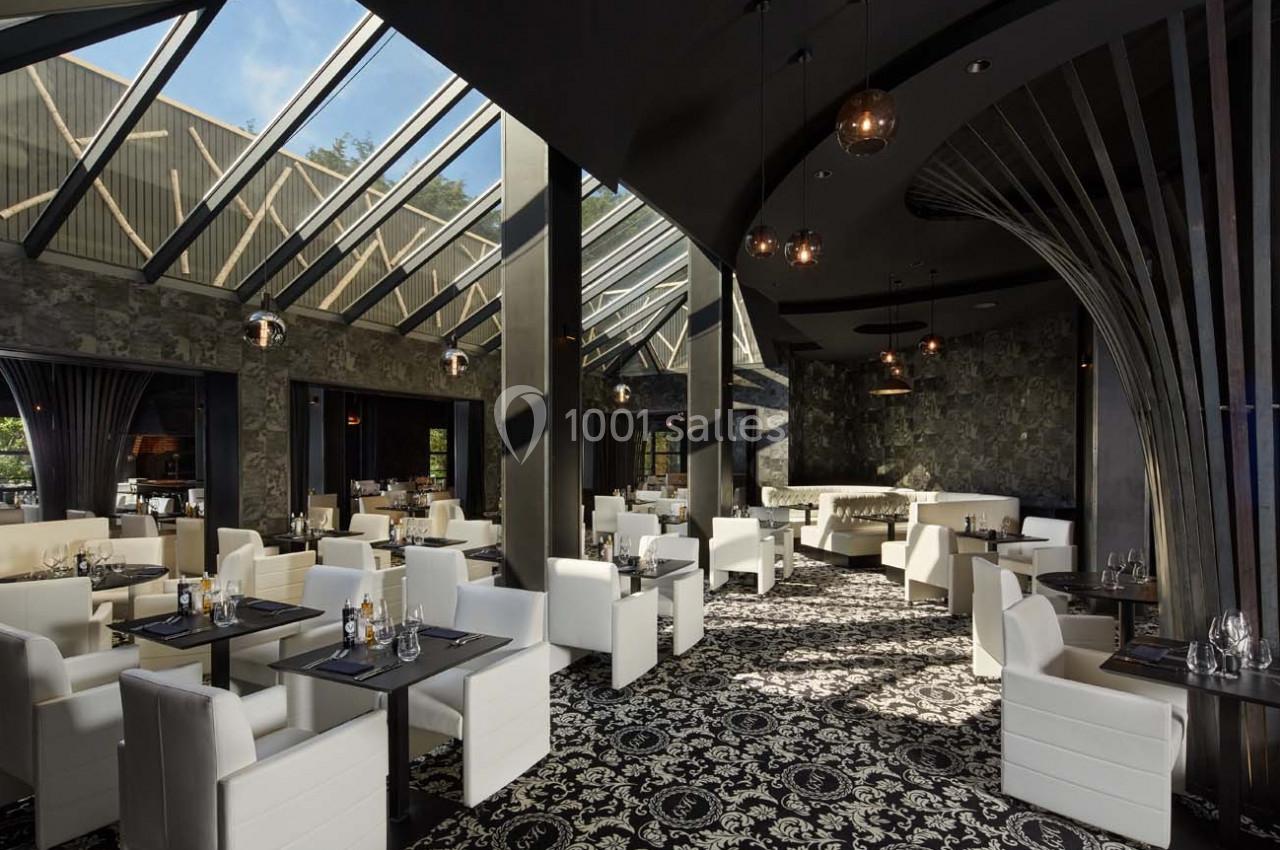 Salle de restaurant moderne avec grandes baies vitrées, mobilier blanc et décorations sombres et élégantes.