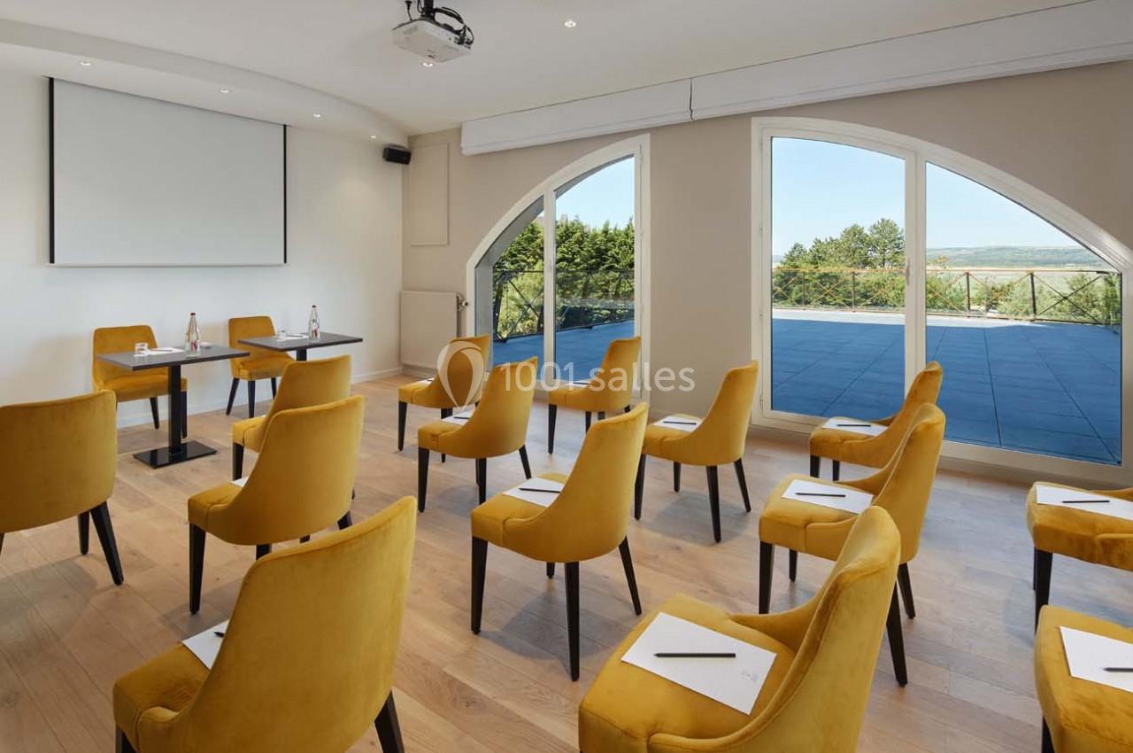 Salle de réunion lumineuse avec chaises jaunes, tables équipées de carnets et stylos, et vue sur une terrasse extérieure.