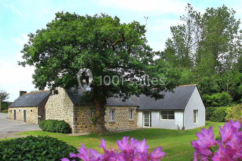 Maison en pierre avec extension moderne, entourée d'un jardin verdoyant et d'un grand arbre, vue sous un ciel dégagé.