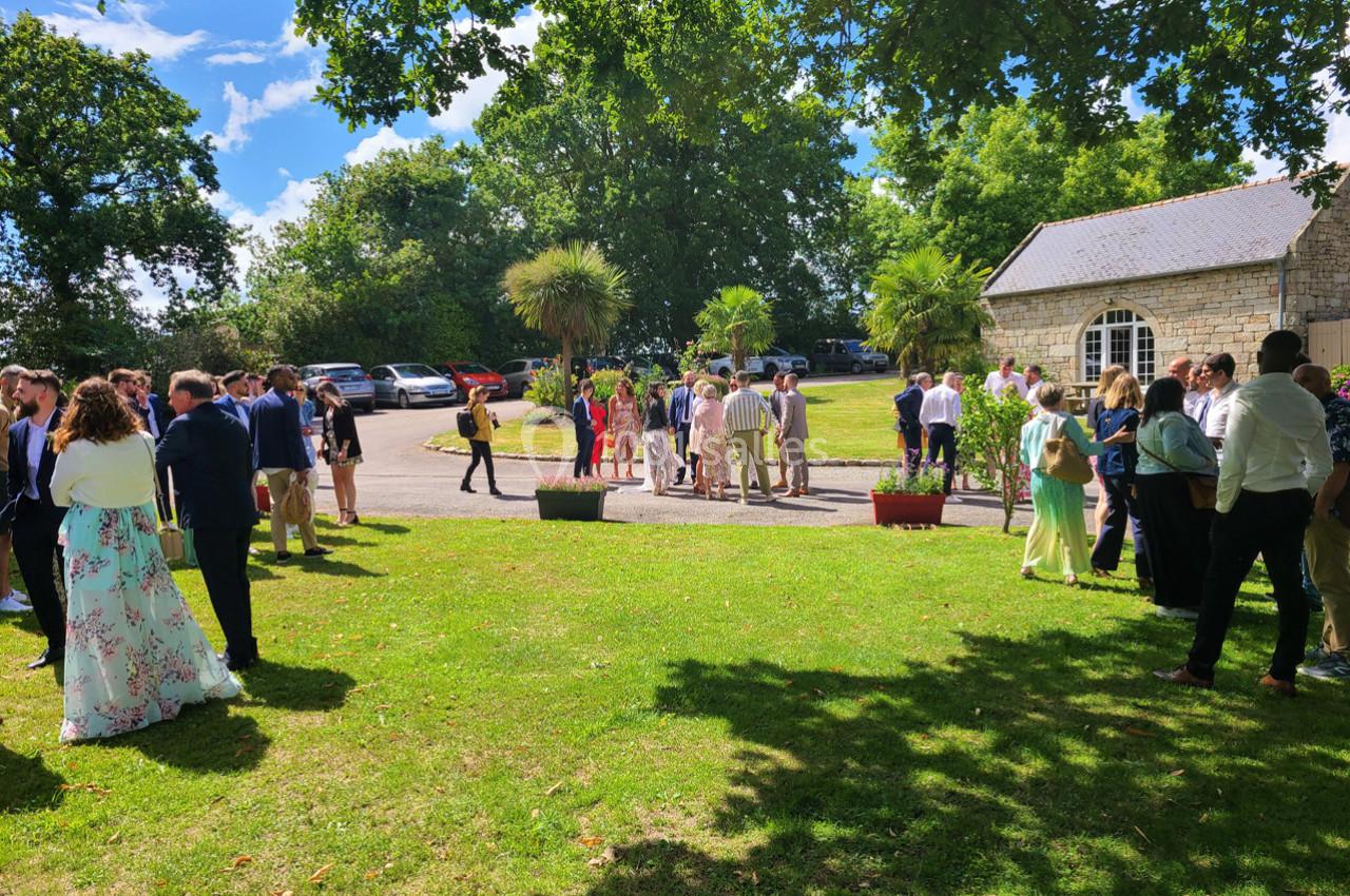 Groupe de personnes rassemblées dans un jardin verdoyant près d'un bâtiment en pierre par une journée ensoleillée.