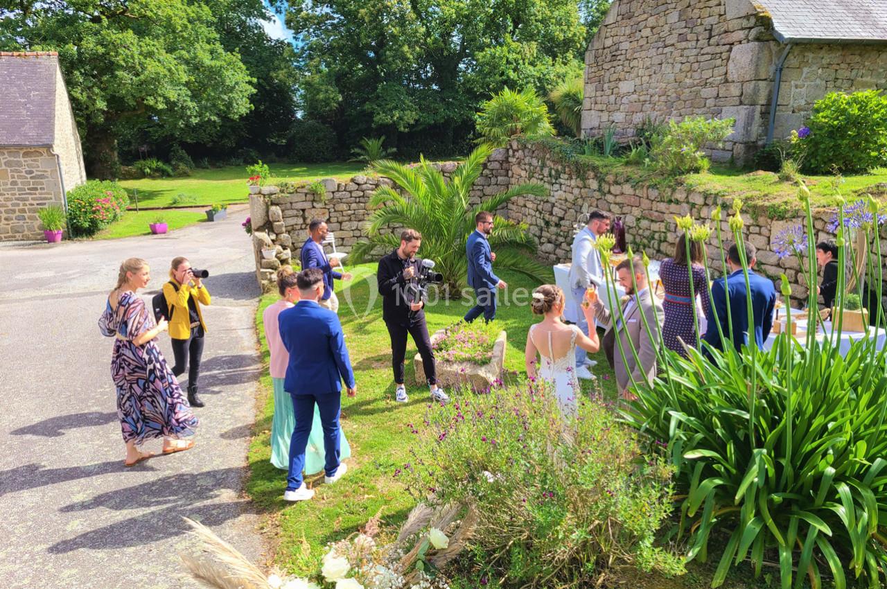 Groupe de personnes rassemblées en extérieur près d'un bâtiment en pierre, entouré de verdure et de fleurs.