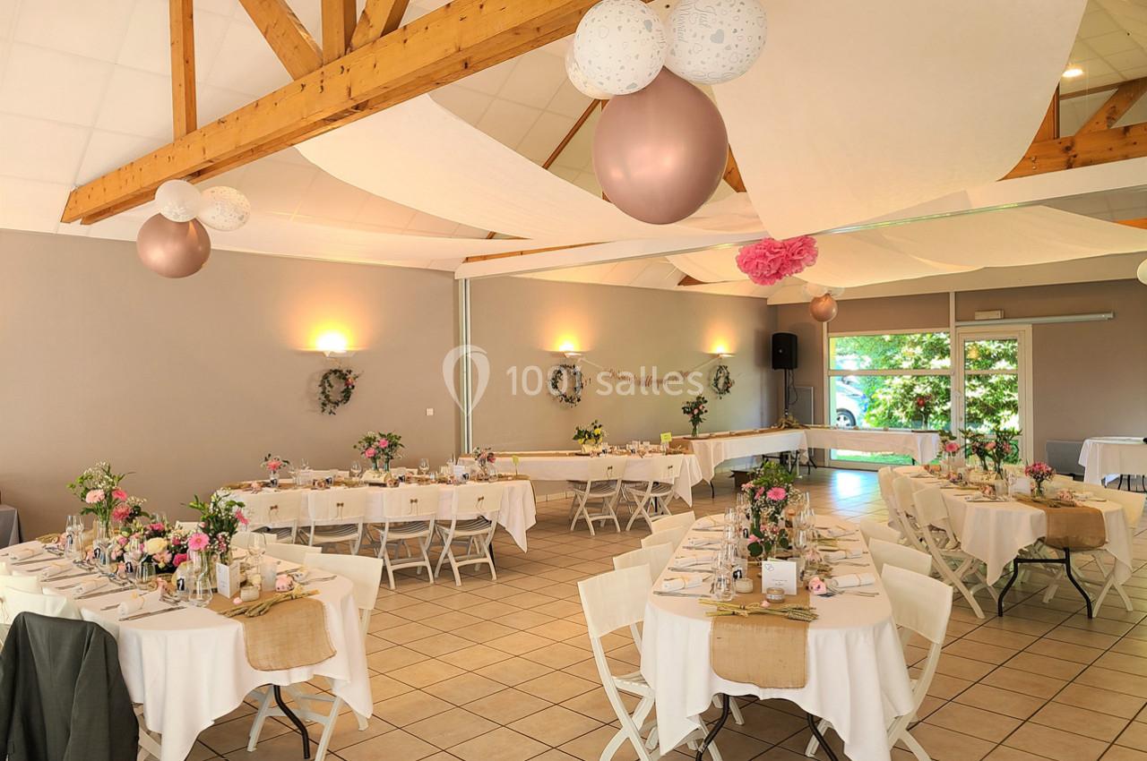 Salle de réception décorée pour un événement, avec tables dressées, fleurs, ballons et éclairage chaleureux.