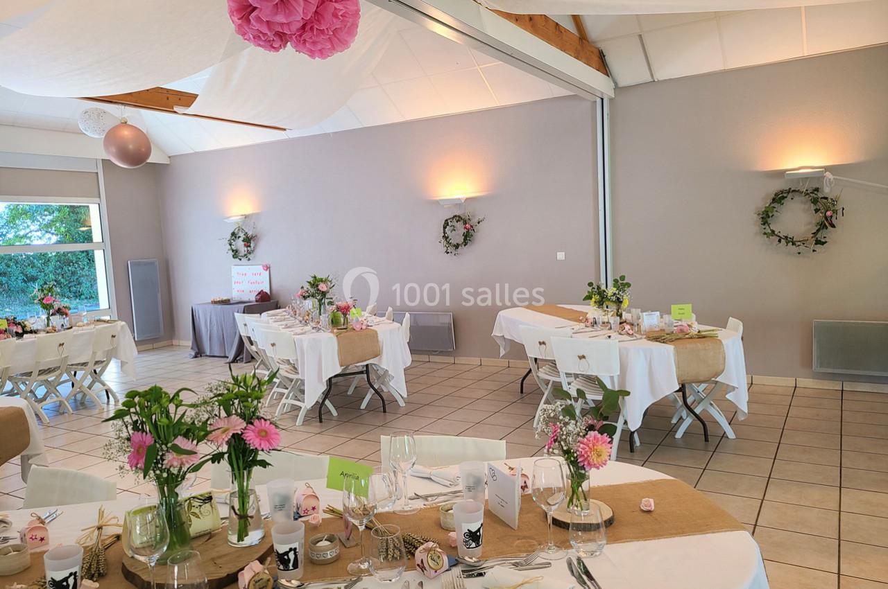 Salle décorée pour une réception avec tables dressées, nappes blanches, fleurs roses et éléments en toile de jute.