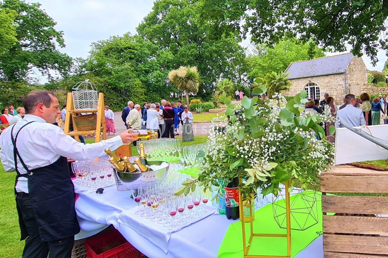 Serveur préparant des boissons sur une table dressée en extérieur lors d'un événement convivial dans un jardin.