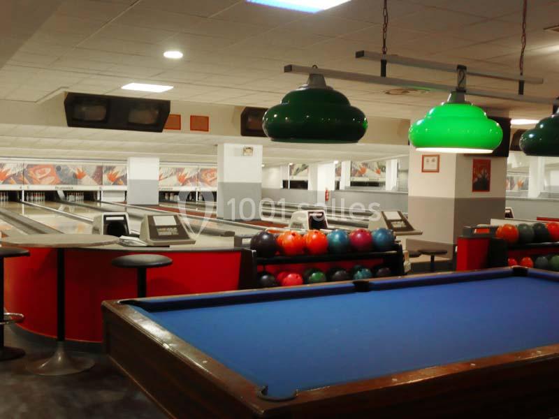 Salle de loisirs avec un billard au premier plan et des pistes de bowling en arrière-plan.