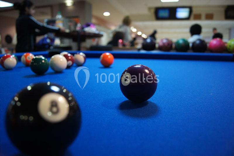 Billard avec des boules colorées sur une table bleue, arrière-plan flou montrant des personnes et un environnement intérieur.