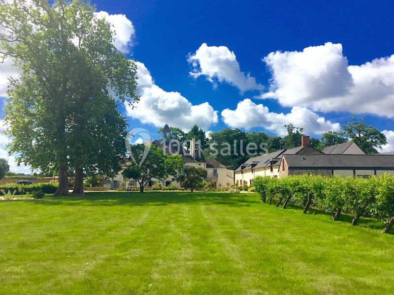Vue d'un grand jardin verdoyant avec des bâtiments en arrière-plan sous un ciel bleu parsemé de nuages.