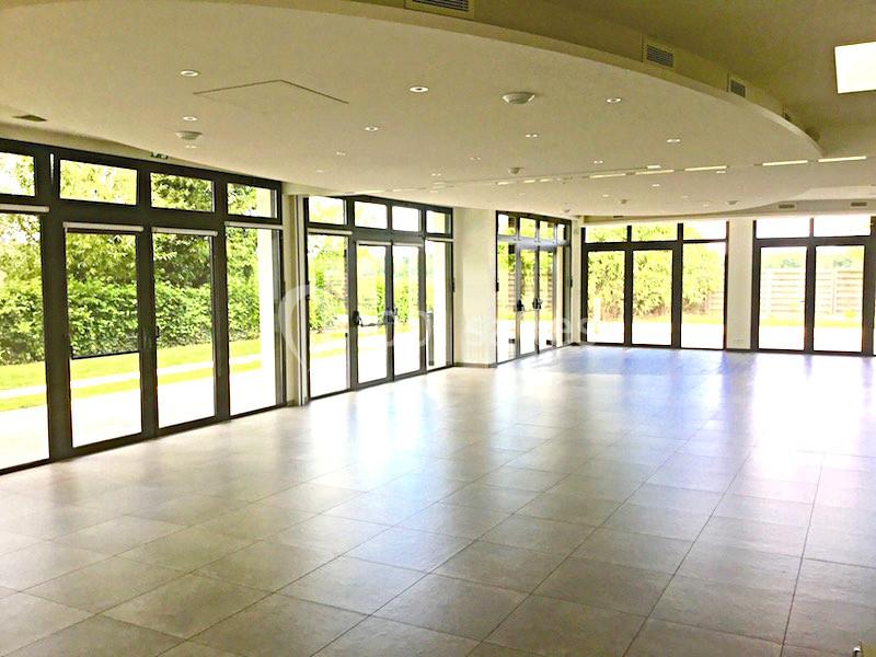 Salle lumineuse avec de grandes baies vitrées donnant sur un espace extérieur verdoyant, sol en carrelage clair.