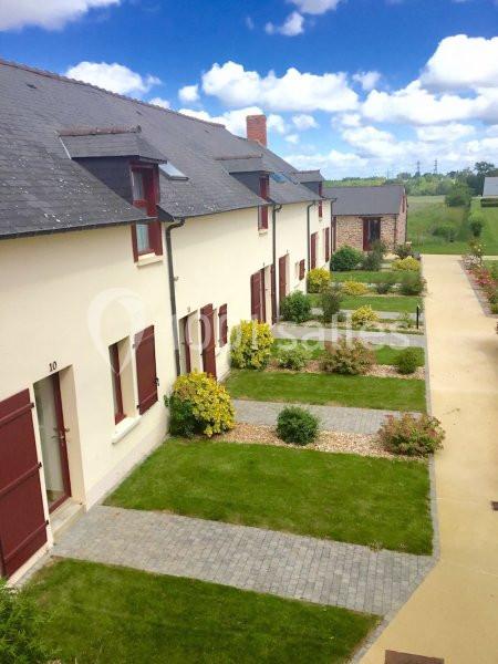 Alignement de maisons mitoyennes avec façades claires, volets rouges, jardins entretenus et allées pavées sous un ciel bleu.