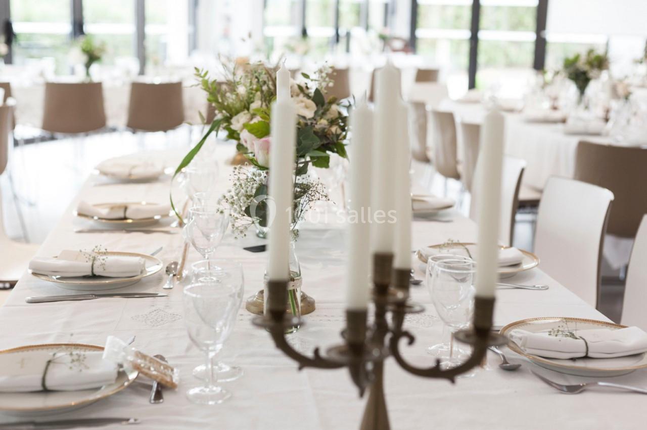 Table élégamment dressée avec nappes blanches, chandeliers, vaisselle raffinée et bouquets de fleurs en centre de table.