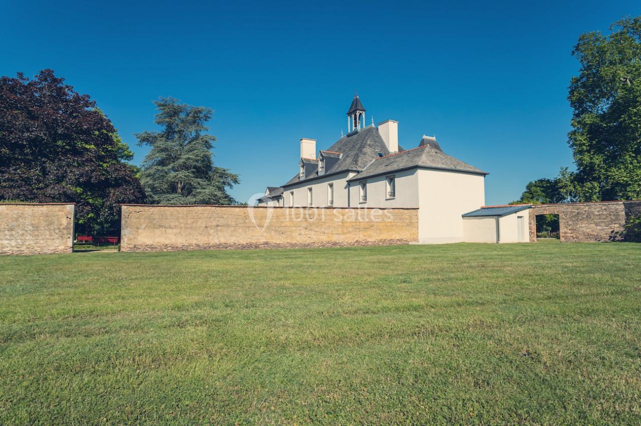 Bâtiment ancien avec clocher, entouré d'un mur en pierre et d'une pelouse, sous un ciel bleu dégagé.