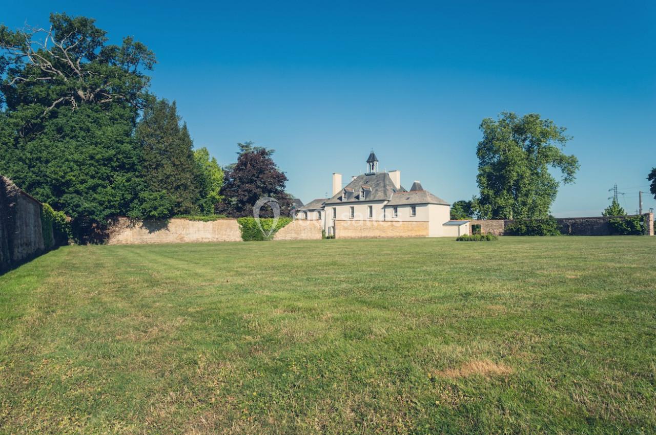 Grand jardin avec pelouse bien entretenue, entouré de murs, et un bâtiment ancien avec un clocher en arrière-plan.