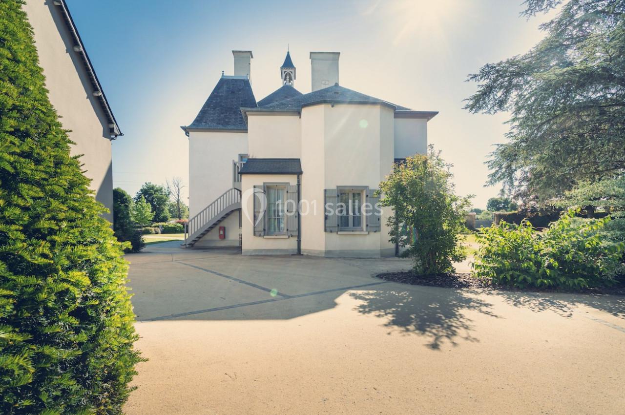 Façade d'une maison blanche à deux étages avec un petit escalier extérieur, entourée de végétation sous un ciel ensoleillé.