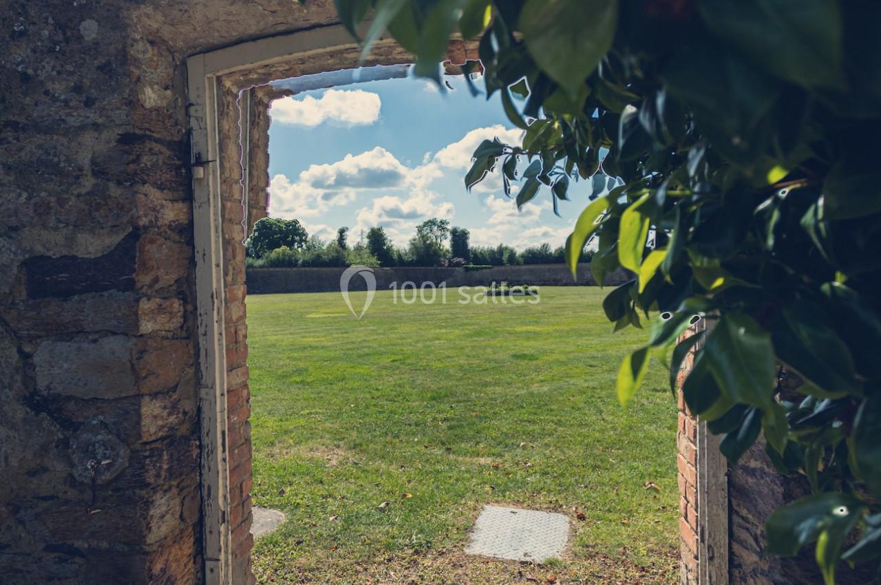 Vue d'un jardin verdoyant à travers une porte en pierre, encadrée par des feuilles et baignée de lumière naturelle.