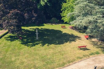 Vue d'un jardin avec pelouse, arbres, bancs rouges et une statue au centre, sous un ciel dégagé.