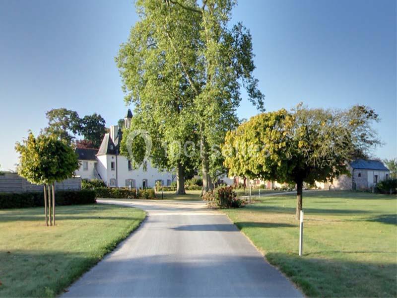 Allée bordée d'arbres menant à une maison blanche entourée de pelouses et de jardins.