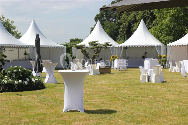 Tentes blanches et tables hautes installées sur une pelouse pour un événement en extérieur par temps clair.