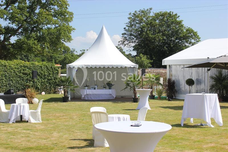 Tente blanche installée sur une pelouse avec des tables et chaises disposées pour un événement en extérieur.